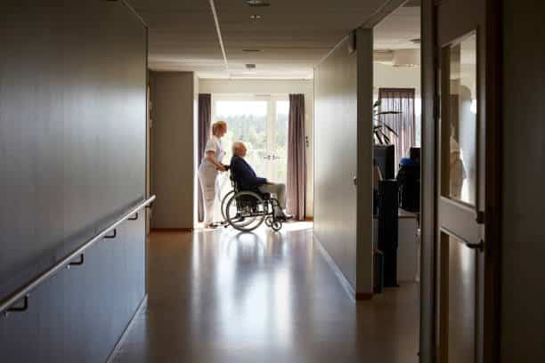 Infirmière en maison de retraite qui accompagne un résident en fauteuil roulant