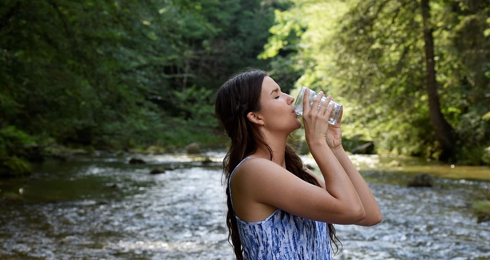 Jeune femme qui boit un verre d'eau au pied d'une source pour ses bienfaits sur la santé