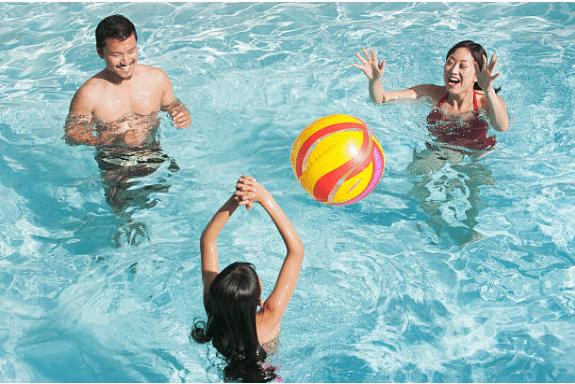 2 adultes et un enfant jouant au ballon dans une piscine